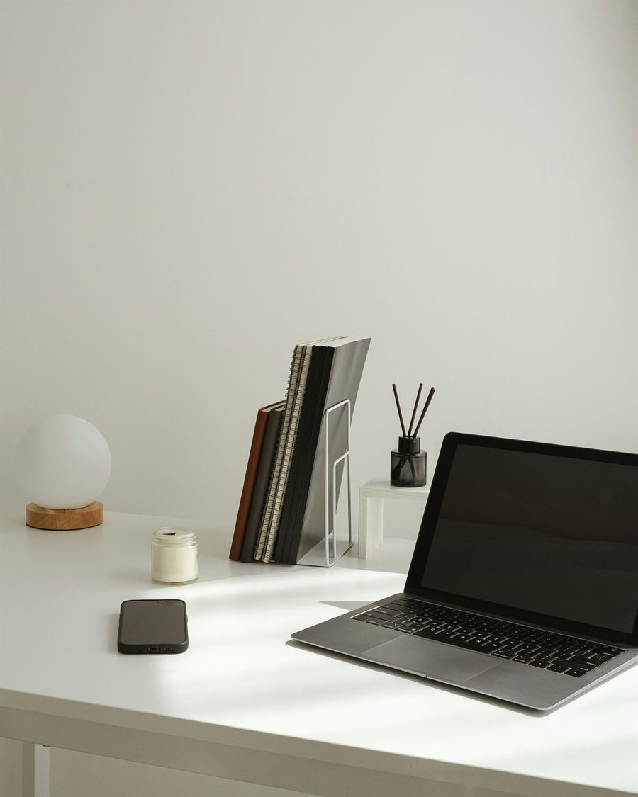 A calm white desk with a laptop, notebooks and a globe lamp in soft daylight, holding the place of the founder portrait