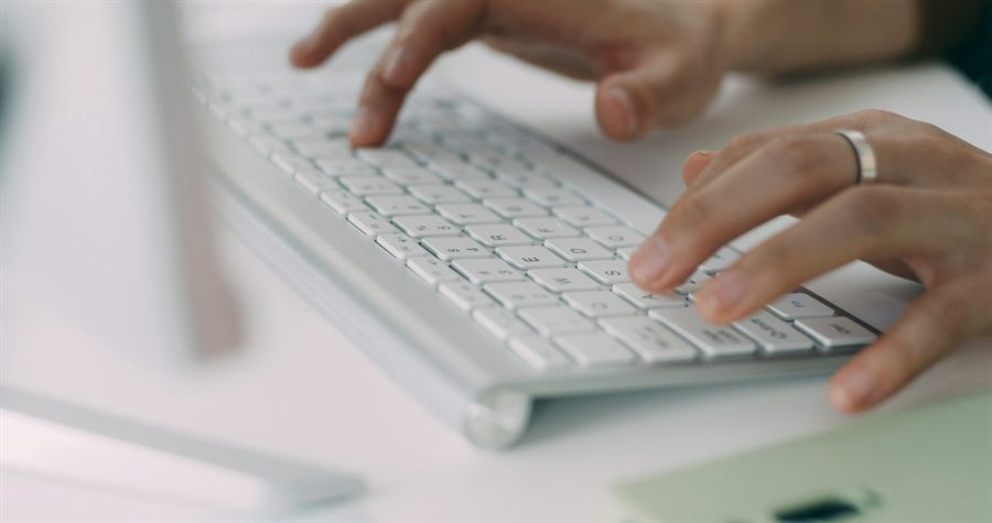 Hands typing on a white keyboard at a bright desk, standing in for an Art-icled draft