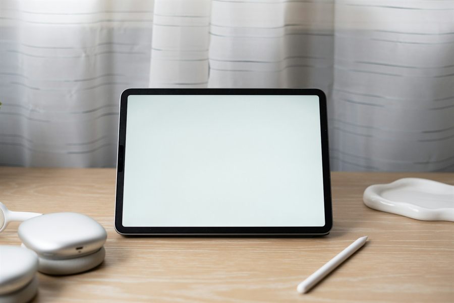 A tablet with a blank screen on a pale oak desk beside a stylus, standing in for the Client Ops Portal
